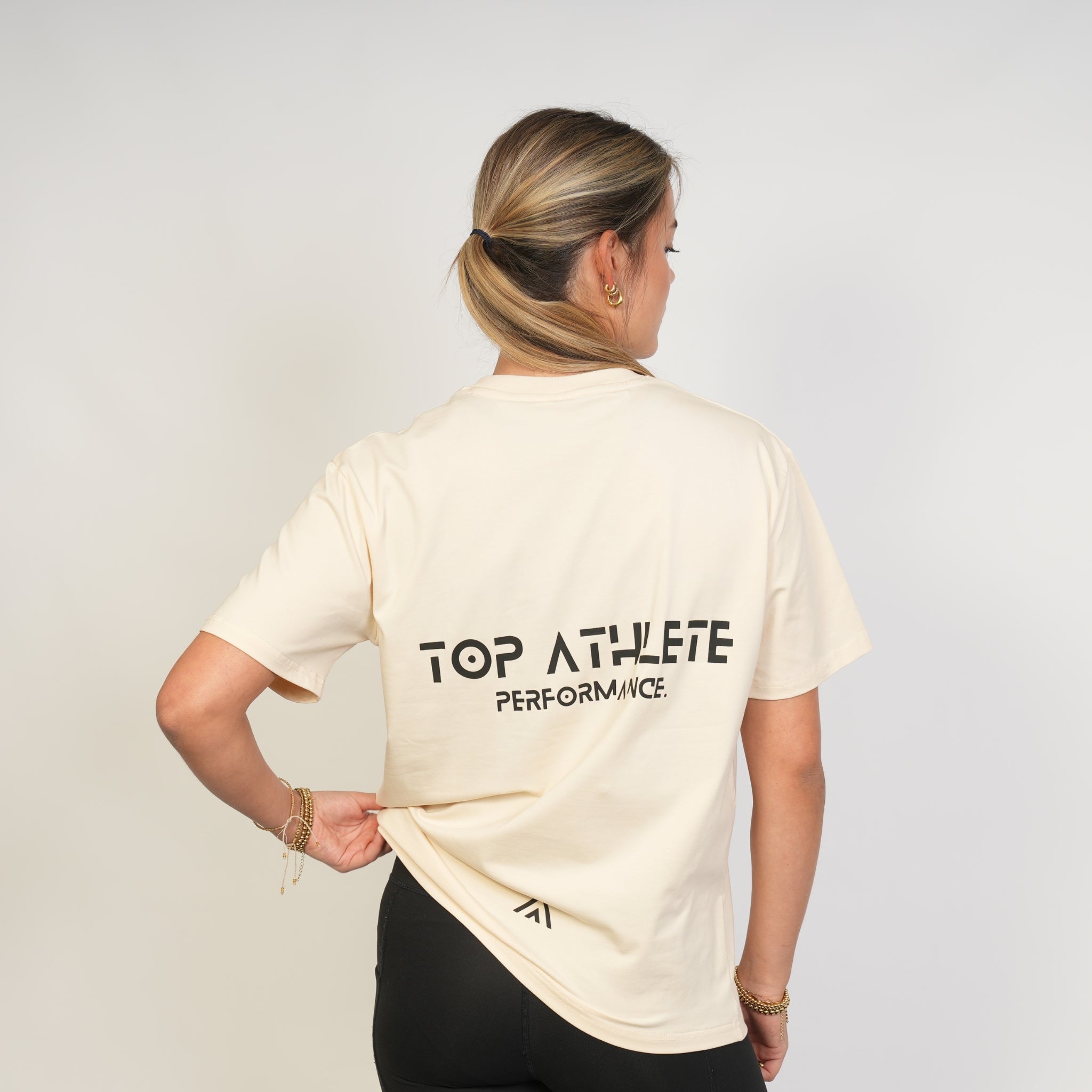 Woman wearing a beige 'Top Athlete Performance' t-shirt on a plain background